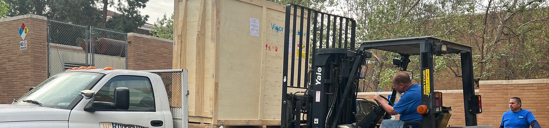 A Receiving Services worker uses a forklift to load a crate onto a flatbed truck.